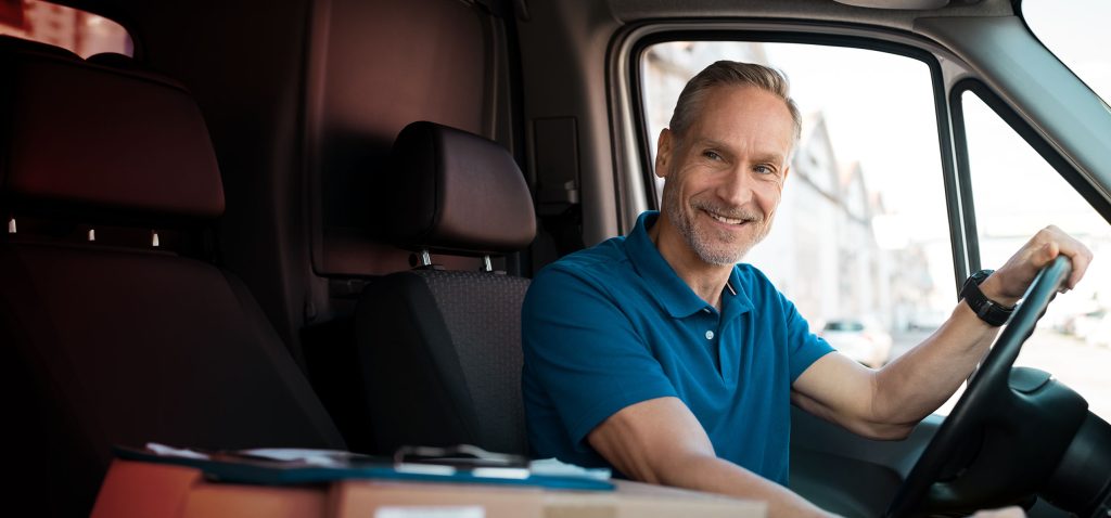 Delivery man driving van with packages on the front seat. Happy mature courier in truck. Portrait of confident express courier driving his delivery van.